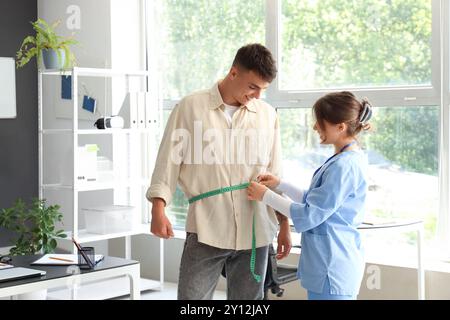 Ernährungsberaterin, die die Taille des Mannes in der Klinik misst Stockfoto