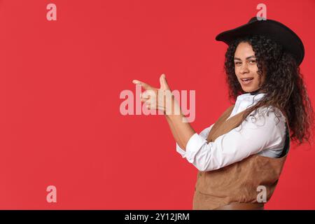 Afroamerikanisches Cowgirl macht Waffe mit ihren Händen auf rotem Hintergrund Stockfoto