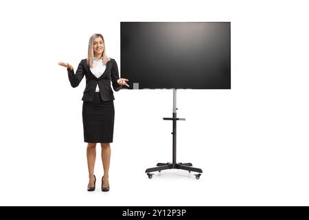 Porträt einer professionellen Frau in einem Anzug, die vor einem fernseher auf weißem Hintergrund präsentiert Stockfoto