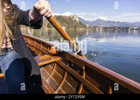 Junge Frau, die auf einem Holzboot paddelt, der Bleder See in Slowenien rudert an einem sonnigen Tag auf Holzbooten Stockfoto