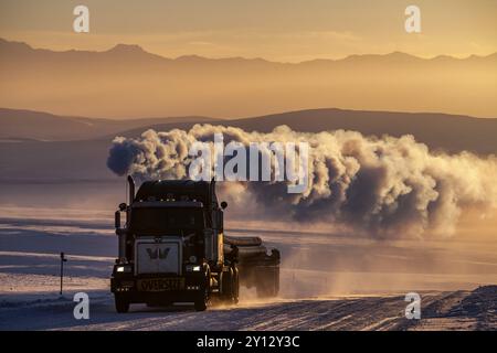 Lkw auf verschneiten Strecken mit großer Abluftwolke vor Bergen im Winter, Abendlicht, Dalton Highway, Alaska Stockfoto