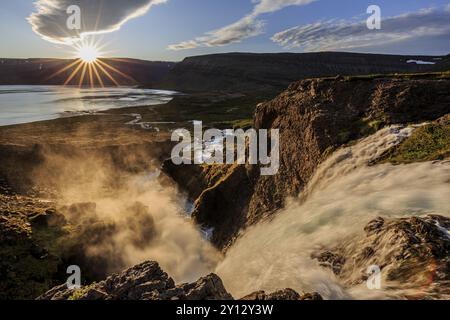 Wasserfall mit Hintergrundbeleuchtung von Mitternachtssonne vor Bergen und Küste, Sommer, Dynjandi, Westfjorde, Island, Europa Stockfoto