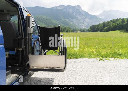 Foto des Spezialfahrzeugs für den Elektroaufzug in Schwarz für Menschen mit Behinderungen. Leerer Rollstuhl auf einer Rampe mit Natur und Bergen im Rücken Stockfoto