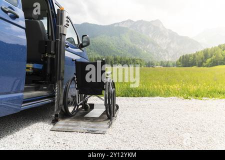 Foto des Spezialfahrzeugs für den Elektroaufzug in Schwarz für Menschen mit Behinderungen. Leerer Rollstuhl auf einer Rampe mit Natur und Bergen im Rücken Stockfoto