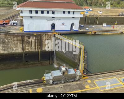 Schleuse mit einer Lokomotive auf Schienen vor einem Gebäude. Der Kanal ist ruhig und der Himmel ist klar, panama Stadt, Panamakanl, panama, Zentralamerika Stockfoto