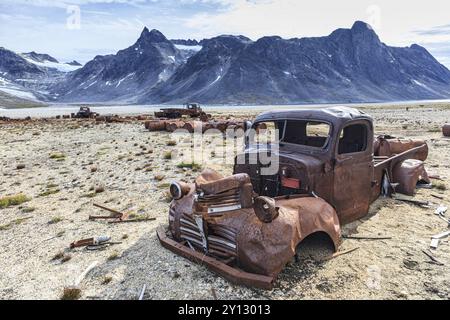 Rostige Autos und Ölfässer vor steilen Bergen, Überreste eines US-Luftwaffenstützpunktes aus dem Zweiten Weltkrieg, Ikateq Fjord, Ostgrönland, Grönland, Nort Stockfoto