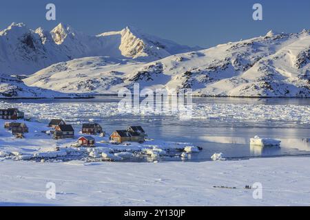 Inuit Siedlung, Häuser am Fjord mit Eisbergen vor verschneiten Bergen, Winter, sonnig, Kulusuk, Ostgrönland, Grönland, Nordamerika Stockfoto