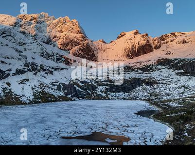 Aus der Vogelperspektive auf den eisigen See vor den steilen Bergen, Winter, Sonnenaufgang, Storvatnet, Flakstadoya, Lofoten, Norwegen, Europa Stockfoto