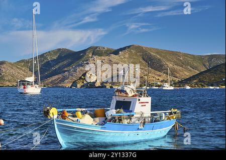 Farbenfrohes Fischerboot auf blauem Wasser, mit Bergen und bewölktem Himmel im Hintergrund, Petras Beach, Kalikatsou Rocks, Patmos, Dodekanese, Griechischer Islan Stockfoto