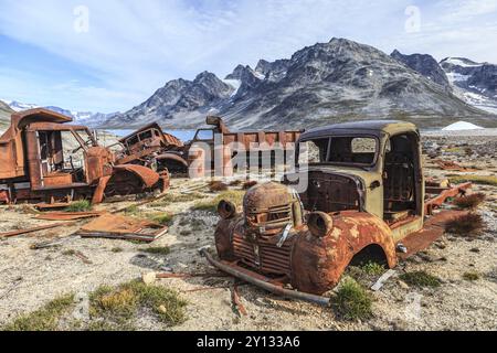 Rostige Autos und Ölfässer vor steilen Bergen, Überreste eines US-Luftwaffenstützpunktes aus dem Zweiten Weltkrieg, Ikateq Fjord, Ostgrönland, Grönland, Nort Stockfoto