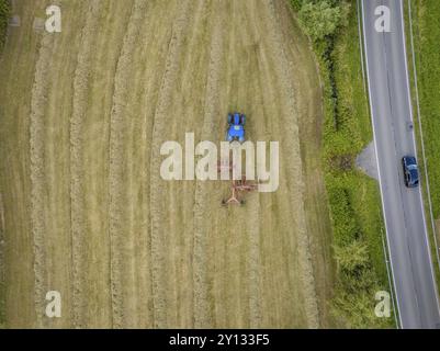 Aus der Vogelperspektive eines Traktors mit heuzange auf einem Heufeld neben einer Landstraße, umgeben von Bäumen, Dachtel. Schwarzwald, Deutschland, Europa Stockfoto