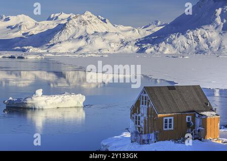 Typisch grönländisches Haus vor Eisbergen, Fjord und verschneiten Bergen, sonnig, Inuit Siedlung, Winter, Arktis, Kulusuk, Ostgrönland, Grönland Stockfoto