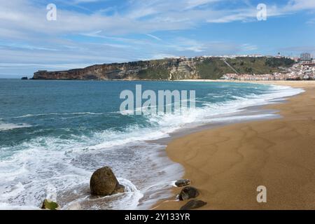 Blick auf die Strandküste von Nazare mit Wellen, Sand und einem malerischen Hügel im Hintergrund, Praia da Nazare Strand, Nazare, Oeste, Leiria Bezirk, CE Stockfoto