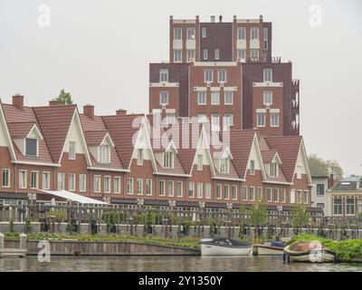 Moderne Reihenhäuser und ein mehrstöckiges Gebäude an einem Wasserkanal mit Booten im Vordergrund, Leiden, Niederlande Stockfoto