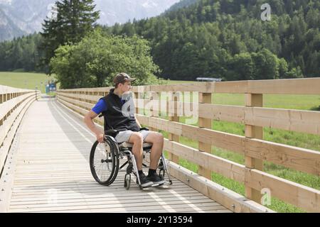 Behinderte junge Menschen auf einen Rollstuhl auf einer hölzernen Brücke weg Genießen in der Natur schöne Aussicht suchen Stockfoto