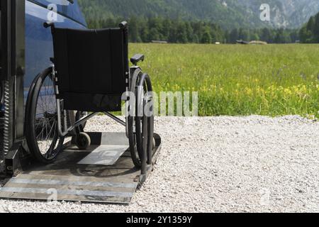 Foto des Spezialfahrzeugs für den Elektroaufzug in Schwarz für Menschen mit Behinderungen. Leerer Rollstuhl auf einer Rampe mit Natur und Bergen im Rücken Stockfoto