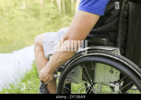 Junger behinderter oder behinderter Mann, der in der Natur auf einem Rollstuhl sitzt und Räder hält Stockfoto