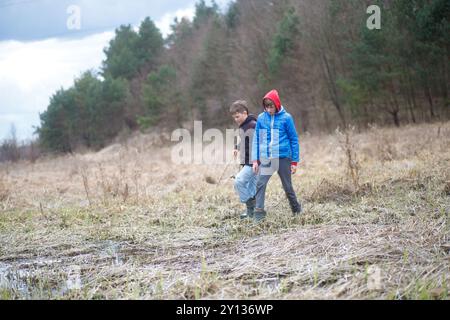 Zwei Jungen erkunden an einem bewölkten Tag eine grasbewachsene Gegend in der Nähe eines kleinen Teichs im Wald Stockfoto