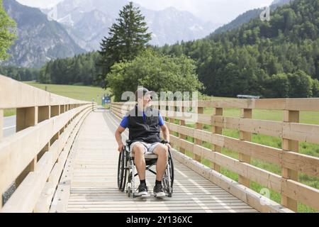 Behinderte junge Menschen auf einen Rollstuhl auf einer hölzernen Brücke weg Genießen in der Natur schöne Aussicht suchen Stockfoto