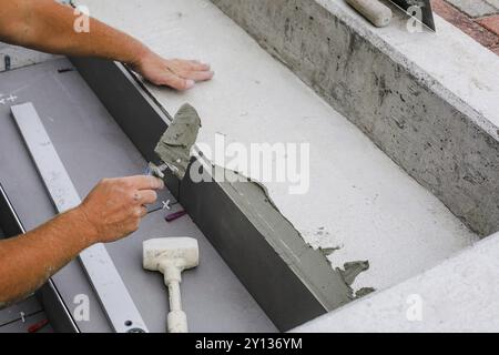 Fliesenhände arbeiten an einem neuen Hauseingang, lokaler und professioneller Handwerker, der Fliesen auf die Stufen aufbringt Stockfoto