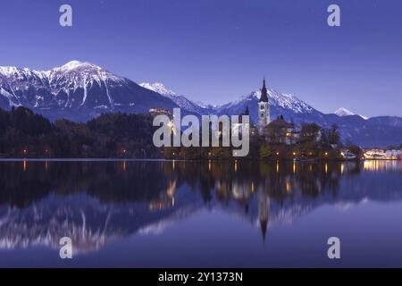 Malerischer Blick auf den See im Winter Nacht mit Castle Rock und St. Martin Kirche unter schöner Sternenhimmel im See Wasser spiegelt Bled Stockfoto