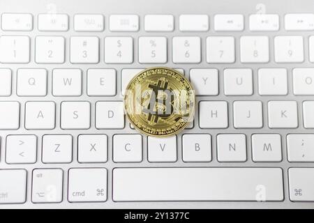 Foto von goldenem Bitcoin in Cyptowährung, der auf weißer Tastatur im Hintergrund liegt. Symbol für elektronisches virtuelles Geld Stockfoto