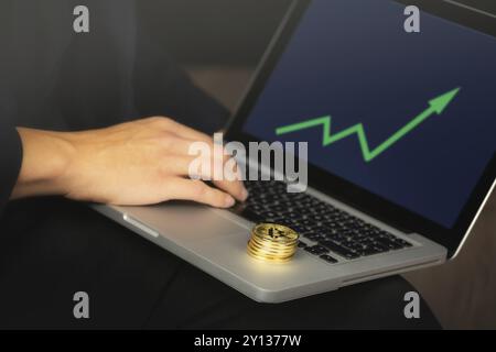 Geschäftsmann, der an einem Laptop arbeitet, auf dem sich goldene Bitcoin-Münzen befinden. Green Chart, Konzept der Preiserhöhung Stockfoto