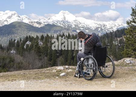 Foto eines Mannes im Rollstuhl mit Kamera in der Natur, der wunderschöne Berge fotografiert Stockfoto