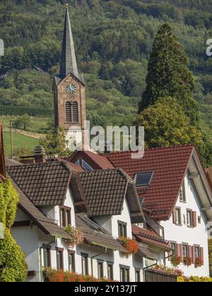 Panorama eines Dorfes mit Kirche und Uhrenturm, roten Ziegeldächern, grünen Bäumen und bewaldeten Hügeln im Hintergrund, Schwarzwald, Bade-Württemberg, GE Stockfoto