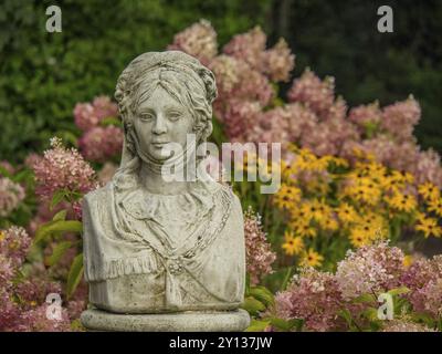 Steinbüste einer Frau in einem blühenden Garten mit rosa und gelben Blumen, spiekeroog, ostfriesland, Nordsee, deutschland Stockfoto