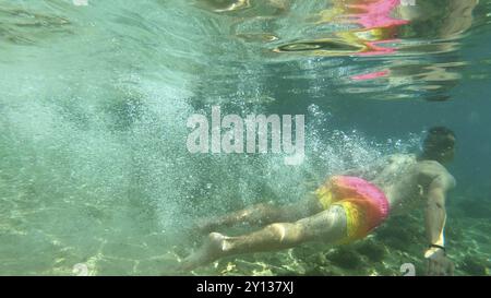 Junger Student männlich springt in und hat im Sommer Spaß im schönen blauen Meer Stockfoto