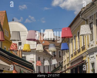 Bunte Lampenschirme zieren eine lebhafte Straße mit historischen Gebäuden unter sonnigem Himmel, esztergom, donau, ungarn Stockfoto