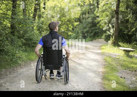 Glücklich und junge behinderte Mann sitzt auf einem Rollstuhl in der Natur drehen die Räder auf einer gehenden Straße an einem sonnigen Tag Stockfoto