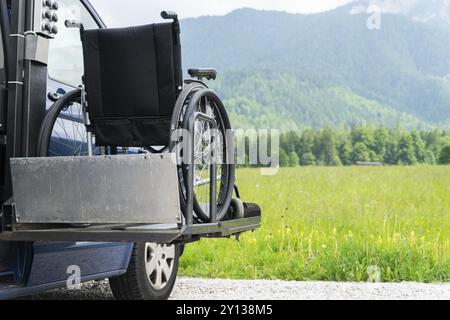 Foto des Spezialfahrzeugs für den Elektroaufzug in Schwarz für Menschen mit Behinderungen. Leerer Rollstuhl auf einer Rampe mit Natur und Bergen im Rücken Stockfoto