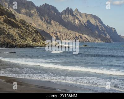 Eine atemberaubende Küstenlandschaft mit zerklüfteten Klippen und Wellen, die unter einem blauen Himmel mit Wolken gegen die Küste krachen, teneriffa, kanarische Inseln, spanien Stockfoto