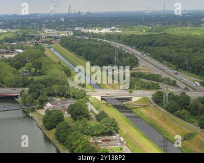 Eine Autobahn und ein parallel verlaufender Kanal, eingebettet in grüne Bäume. Vogelperspektive der Industriegebiete im Hintergrund, oberhausen, ruhrgebiet, Deutsch Stockfoto