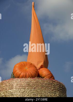 Kürbisstapel auf einem Strohballen, gekrönt von einer orangefarbenen Stofffahne vor einem blauen Himmel, borken, münsterland, deutschland Stockfoto