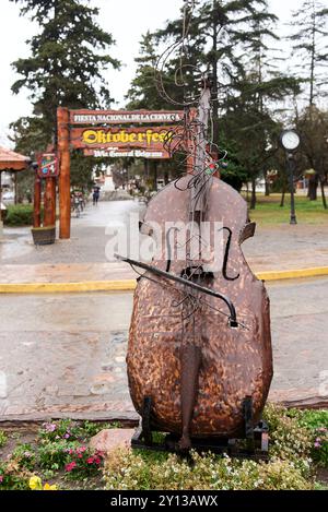 Villa General Belgrano, Cordoba, Argentinien; 20. August 2024: Skulptur eines Kontrabasses, hinter dem Jose Hernandez-Platz mit seinem charakteristischen Bogen Stockfoto