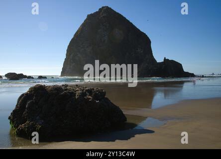 Haystack Rock dominating the horizon along Cannon Beach, with small waves breaking on the beach under a bright sunny summer sky. Stockfoto