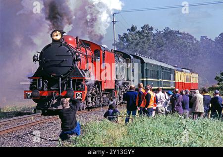 Dampfeisenfreunde fotografieren um 1998 zwei Lokomotiven der M-Klasse, die Wagen an Western Junction in Tasmanien, Australien, gezogen haben. Die Frontlok MA2 wurde 1951 von Robert Stephenson & Hawthorns Ltd. In Newcastle gebaut 7421 und war eine von 10, die von der tasmanischen Regierung in Auftrag gegeben wurden. Stockfoto