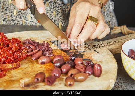 Nahaufnahme von Händen, die Oliven, sonnengetrocknete Tomaten und andere Zutaten auf Holzbrettern in einer Küche schneiden. Stockfoto