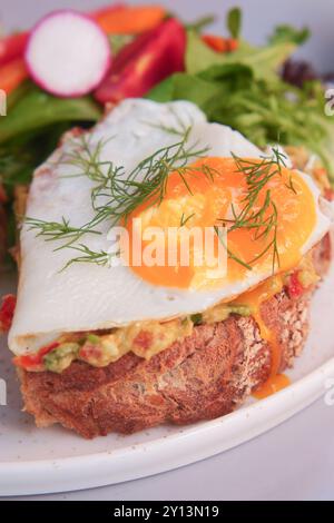 Genießen Sie den köstlichen Avocado Toast mit einem gebratenen Ei, serviert mit einem frischen Salat Stockfoto