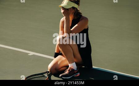 Eine Frau hockte sich auf einem Tennisplatz, weinte, nachdem sie ein Spiel verloren hatte, trug eine Sportmütze und Tenniskleidung. Stockfoto