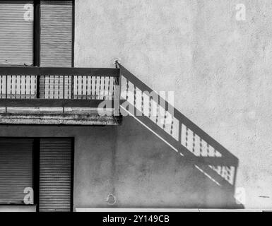 Geschlossene Balkontür mit Jalousien: Abstrakte Treppenschatten und schmutziger Mauerhintergrund. Stockfoto