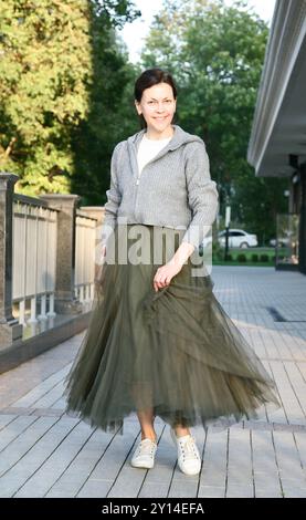 Frau mittleren Alters im modischen grünen Tüllrock lächelt und wirbelt Stockfoto
