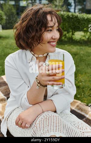 Eine hübsche junge Frau entspannt sich bei einem Sommer-Picknick, schlürft einen kühlen Drink und genießt das sonnige Wetter. Stockfoto