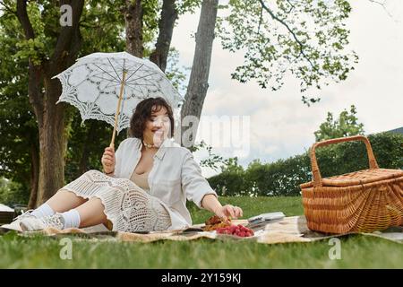 Eine fröhliche junge Frau entspannt sich auf einer Decke und genießt ein köstliches Picknick an einem sonnigen Sommertag. Stockfoto