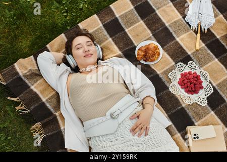 Eine junge Frau in einem weißen Hemd genießt einen ruhigen Moment bei einem sonnigen Picknick, umgeben von Snacks. Stockfoto