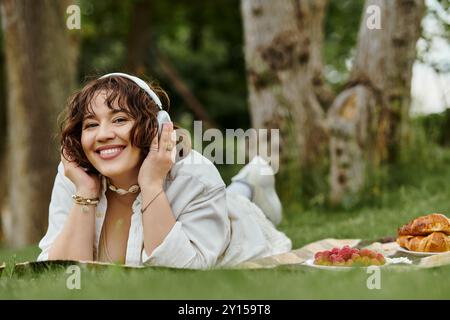 Eine fröhliche junge Frau entspannt sich auf einer Decke und genießt die Freuden des Sommers mit einem leckeren Picknick-Aufstrich. Stockfoto