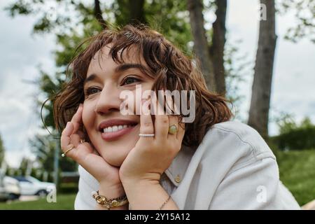 Eine fröhliche junge Frau in einem weißen Hemd entspannt sich und genießt die Wärme des Sommers unter einem Baumdach. Stockfoto